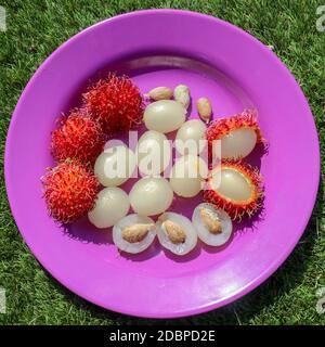 Primo piano di rambutan, frutti interi e pelati. Vista dall'alto frutta sana su sfondo viola. Pronto a mangiare la dolce frutta di Bali. La frutta è ovale arrotondato Foto Stock