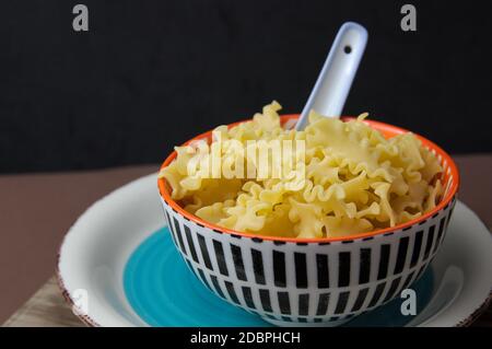Una ciotola con pasta corta italiana cruda conosciuta come corta mafalda su sfondo scuro con spazio per la copia Foto Stock