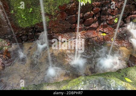 Sorgenti d'acqua sacra nella Valle Pakerisan presso il complesso di sepoltura di Tampaksiring. Gunung Kawi, Bali, Indonesia. L'acqua cade sulla superficie dell'acqua e cade Foto Stock