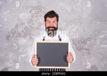 ragazzo maturo con barba e baffi è chef professionista dimostrare cucina menu in caffetteria su lavagna vuota, catering. Foto Stock