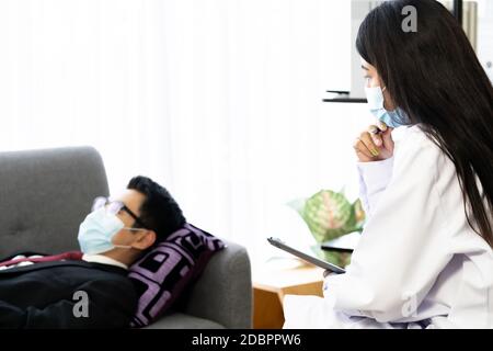 Psicoterapeuta medico femminile che vistano la casa paziente lavorando con depresso uomo d'affari asiatico che si trova su poltrona divano in soggiorno per consultare abo Foto Stock
