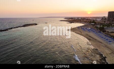 Vista aerea del tramonto sulla costa e della spiaggia simbolo di Agia Thekla, Ayia Napa, Famagosta, Cipro dall'alto. Vista dello skyline dall'alto dell'attrazione turistica Foto Stock