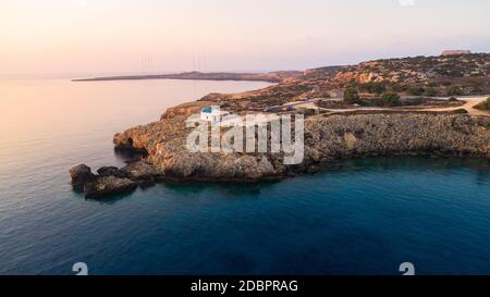 Vista aerea del tramonto della costa e simbolo bianco cappella Agioi Anargyroi, a cavo Greco Protaras, Famagosta, Cipro dall'alto. Vie dell'occhio dell'uccello Foto Stock