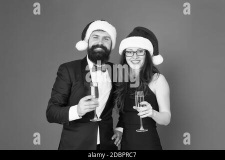 Festa di Natale del tempo. formale di coppia in amore festeggiare il nuovo anno. tuxedo uomo con la donna a santa hat. Buon Natale e saluti a tutti. business man e ragazza bere champagne. xmas party. Foto Stock