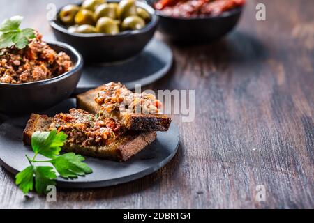 Crostini croccanti con tapenade e ingredienti. Tapenade - deliziosa pasta d'oliva francese. Foto Stock