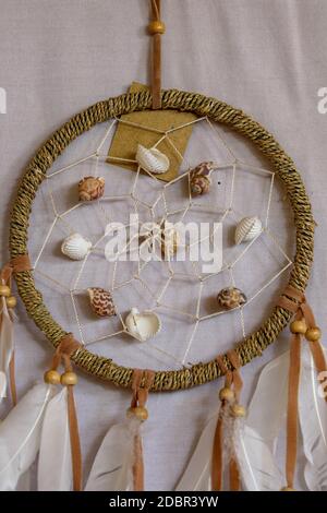 decorazione conchiglia mare. catcher sogno. Catcher da sogno americano nativo di colore rosa fatto a mano sullo sfondo di rocce e lago. Elementi tribali, piume, conchiglie, l Foto Stock
