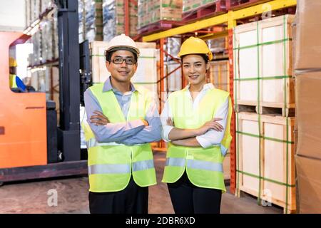 Ritratto del responsabile magazzino asiatico e braccio di lavoro attraversato con il lavoratore di magazzino azionare carrello elevatore a forche per controllare l'inventario in background. Riapertura dell'azienda Foto Stock