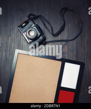 Fotocamera retrò e cornice fotografica vuota su sfondo tavola in legno vintage. Vista dall'alto. Disposizione piatta. Foto Stock