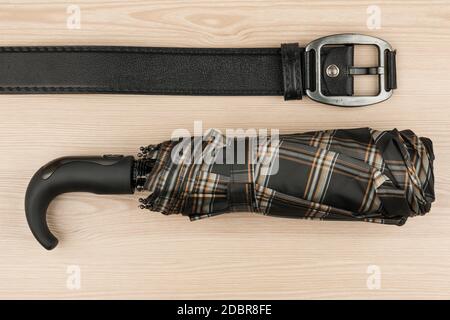 Ombrellone e cinturino in vera pelle giacciono su una superficie in legno, vista dall'alto Foto Stock