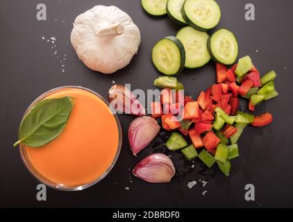 Gazpacho in due bicchieri, con i suoi ingredienti, pomodoro, aglio, cetriolo, pepe rosso e pepe verde. Vista dall'alto. Foto Stock