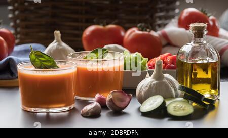 Gazpacho in due bicchieri, con i suoi ingredienti, pomodoro, aglio, olio, cetriolo, pepe rosso e pepe verde. Foto Stock