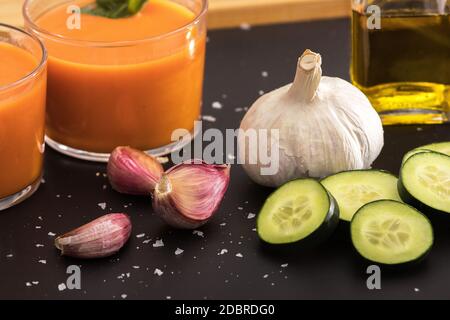 Gazpacho in due bicchieri, con i suoi ingredienti, pomodoro, olio, aglio, cetriolo, pepe rosso e pepe verde. Foto Stock