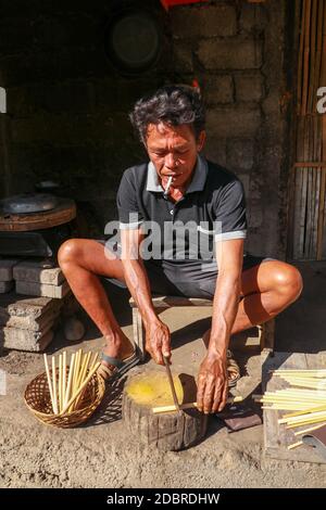 L'uomo anziano sta tagliando il bambù nel suo laboratorio per fare le cannucce di bambù, Bali, Indonesia. Vista frontale ad un lavoratore che fa cannucce di bambù. Foto Stock