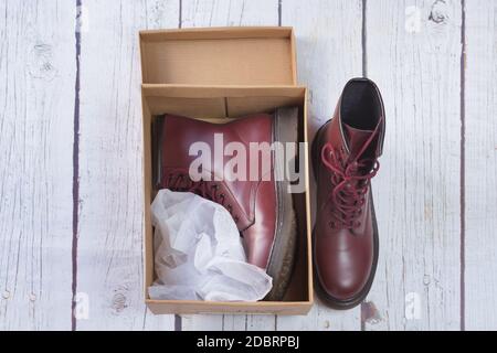 Stivali militari di garnet maroon all'interno di una scatola di cartone, su fondo di legno bianco Foto Stock