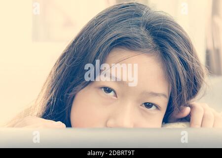 Carina ragazza asiatica sbirciando di cuscini sul divano Foto Stock