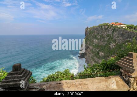 Vista della scogliera di Uluwatu con padiglione e mare blu a Bali, Indonesia. Splendido scenario del tempio pura Luhur Uluwatu con fiori colorati in primo piano d Foto Stock