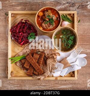 Brodo tradizionale ucraino borscht e vegetale in tazze di carta, insalata di barbabietole in una ciotola di vetro, pane grattugiato e cipolle verdi su un rustico vassoio di legno UK Foto Stock