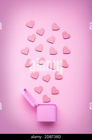 Confezione regalo in metallo rotonde rosa con piccoli cuori in legno su un delicato sfondo rosa. Vista dall'alto Foto Stock