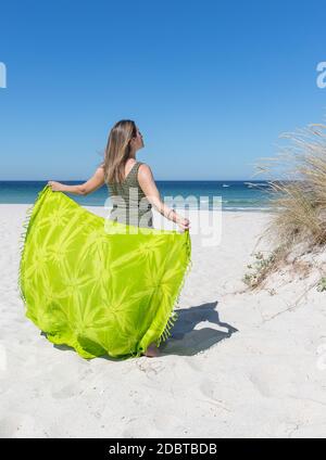 Una donna bionda di mezza età sulla schiena che tiene un verde sarong sulla spiaggia Foto Stock