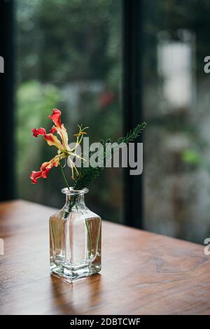 Fiore con foglia in vaso di vetro su tavolo interno in legno con sfondo verde sfocato del giardino Foto Stock