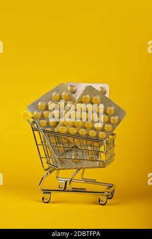 Primo piano diversi blister confezioni di pillole in piccolo carrello di shopping su sfondo giallo, concetto di online medicina ordine di consegna, angolo basso Foto Stock