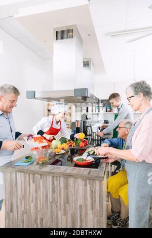 Chef e gruppo di persone che tagliano verdure e cucinano insieme in cucina di addestramento Foto Stock