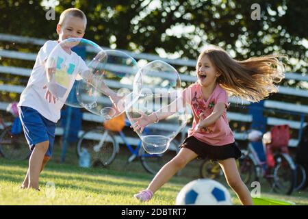 I bambini allegri giocano con enormi bolle di sapone all'aperto, allegra infanzia. Foto Stock