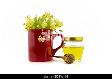 Fiori e foglie di tiglio fresco in una tazza rossa vicino al bacchetta di legno appoggiata su un vaso di vetro di miele su sfondo bianco, concep di guarigione alternativa Foto Stock