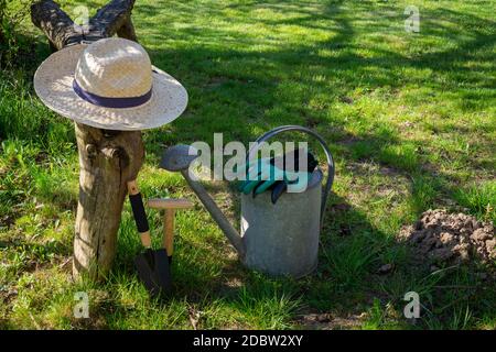 Cappello da sole con guanti, lattina d'irrigazione e attrezzi da giardinaggio adagiato su un prato verde in un giardino primaverile al sole concettuale delle stagioni Foto Stock