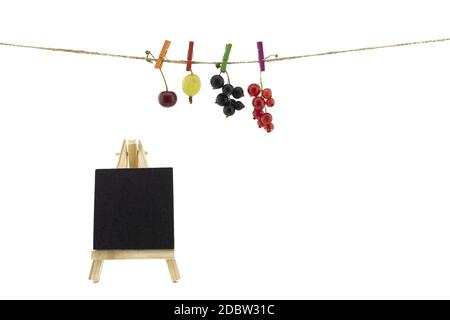 Frutta fresca appesa ai vestiti pesti su una corda con una ciliegia fresca, uva spina, rosso e nero ribes e lavagna di ardesia isolato su bianco con co Foto Stock