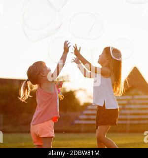 Due ragazze graziose stanno giocando all'aperto con enormi bolle di sapone. Foto Stock