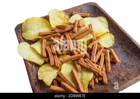 Deliziosi patatine e cracker di pane di segale salato su un piatto di legno scuro, isolati su uno sfondo bianco dal taglio. Foto Stock