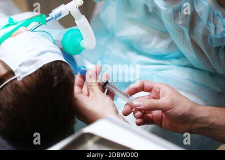 Primo piano della mano di un medico con una siringa. Durante l'operazione, il bambino è sotto anestesia generale. Spazio di copia. Foto irriconoscibile. Foto Stock