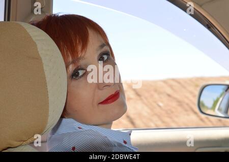 Donna russa a testa rossa seduta sul sedile di un taxi e guardando la macchina fotografica. Foto Stock