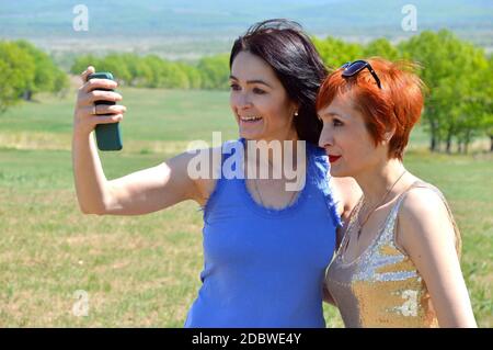 Due sorelle russe che tengono il telefono per parlare con gli amici durante una videochiamata. Ridono sinceramente con i denti Foto Stock