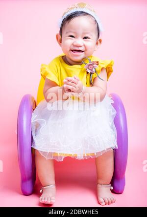 Ritratto di principessa asiatica bambino ragazza felice faccia in bel vestito seduta sulla sedia è un sorriso in studio isolato su sfondo rosa Foto Stock
