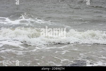 Onde con creste bianche inondare la spiaggia sabbiosa Foto Stock