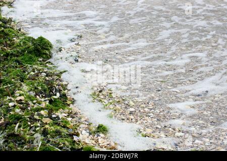 Onde con creste bianche inondare la spiaggia sabbiosa Foto Stock