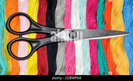 Forbici nere su matasse multicolore di filo interdentale. Scelta di un colore per il lavoro d'ago Foto Stock