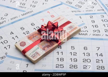 Un fascio di cinque millesimi banconote russe con un arco rosso giace su uno sfondo di un calendario Foto Stock