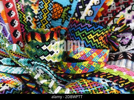 Bracciali di amicizia intrecciati DIY sullo sfondo di molti bracciali di amicizia multicolore fatti a mano di ricamo filo luminoso con nodi. Foto Stock