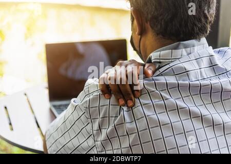 Closeup indietro l'uomo nero asiatico uso mano che tiene la spalla chiropractor davvero male dolore al collo da utilizzare computer portatile che lavora a lungo, infortunio o Foto Stock