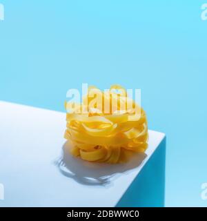 Pasta art. Tagliatelle su piedistallo blu pastello su sfondo blu in luce dura. Un tocco creativo di pasta noodle. Design creativo per menu di ital Foto Stock