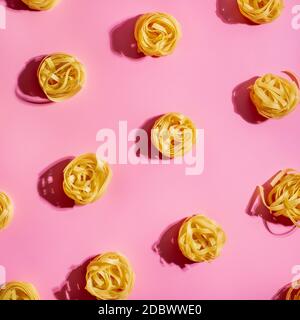 Pasta art. Tagliatelle su fondo rosa in luce dura. Layout creativo con tagliatelle di pasta, vista dall'alto o piatto. Ritaglio quadrato. Design creativo per me Foto Stock