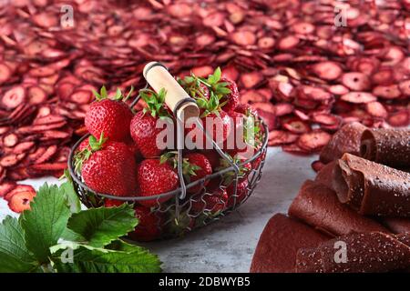 Cesto di metallo con fragole fresche. La pastiglia di fragole viene arrotolata sotto forma di tubi. Sullo sfondo, un gran numero di bacche secche. Natur Foto Stock