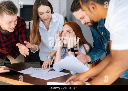 Giovane donna d'affari stanca seduta al tavolo, colleghi multietnici che scuotono i documenti. Foto Stock