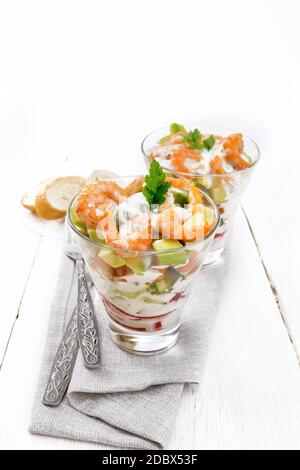 Pasta con insalata di gamberetti, avocado, Fresco cetriolo e peperone e pomodoro condito con salsa di yogurt in due bicchieri di vetro su un asciugamano, pane e delle forcelle Foto Stock