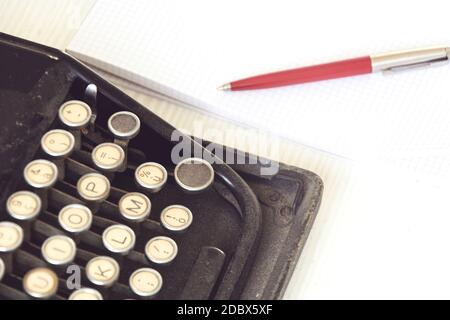 una vecchia macchina da scrivere nera accanto a un foglio di carta bianco con una penna rossa. Giornalismo e strumenti di scrittura. Narrazione e attività creative Foto Stock