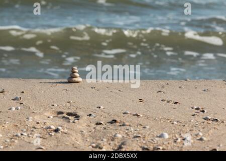 La piramide è fatta di pietre bianche contro lo sfondo delle onde del mare. Stack di ciottoli in riva al mare Foto Stock