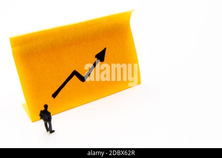 Figurine in miniatura posata come uomo d'affari davanti alla freccia ascendente grafico mano disegnata su carta adesiva nota, immagine di concetto di prestazione positiva Foto Stock